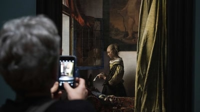 A woman seen taking photos of “Girl Reading a Letter at an Open Window” at Amsterdam's Rijksmuseum, on February 6. Vermeer's use of light — often coming from a window situated on the left of the canvas — the bold colors and meticulous composition can be seen throughout the exhibition, AP reported. (Peter Dejong / AP ) A woman seen taking photos of “Girl Reading a Letter at an Open Window” at Amsterdam's Rijksmuseum, on February 6. Vermeer's use of light — often coming from a window situated on the left of the canvas — the bold colors and meticulous composition can be seen throughout the exhibition, AP reported. (Peter Dejong / AP )