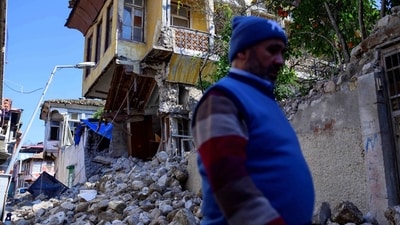 A man walks by the rubble of collapsed buildings in the southern city of Antakya in Turkey, (AFP)