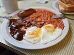 A full English breakfast with eggs, baked beans, bacon, sausage and gravy sauce is served on a table.