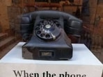 The image shows a rotary telephone kept on a pedestal. The image shows a rotary telephone kept on a pedestal.