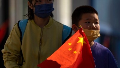 China Population Decline: A boy wearing a face mask carries a Chinese flag as he walks along a pedestrian shopping street in Beijing. (AP) China Population Decline: A boy wearing a face mask carries a Chinese flag as he walks along a pedestrian shopping street in Beijing. (AP)
