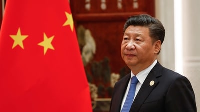 Chinese president Xi Jingping standing next to State flag.