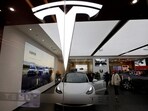 Visitors check a Tesla Model 3 car next to a Model Y displayed at a showroom.