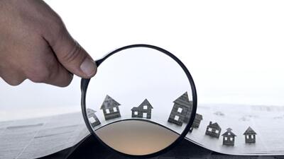 Hand holds the magnifying glass in front of an open newspaper with paper houses. That could mean rent, search, purchase real estate. (Getty Images/iStockphoto) Hand holds the magnifying glass in front of an open newspaper with paper houses. That could mean rent, search, purchase real estate. (Getty Images/iStockphoto)