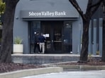 A man puts a sign on the door of the Silicon Valley Bank as an onlooker watches at the bank’s headquarters in Santa Clara, California