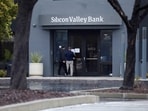 A man puts a sign on the door of the Silicon Valley Bank as an onlooker watches at the bank’s headquarters in Santa Clara, California