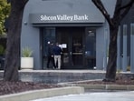 A man puts a sign on the door of the Silicon Valley Bank as an onlooker watches at the bank’s headquarters in Santa Clara, California