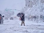 A passer-by uses an umbrella while crossing a snow-covered street, Tuesday, March 14, 2023, in Pittsfield, Mass. The New England states and parts of New York are bracing for a winter storm due to last into Wednesday. (Ben Garver/The Berkshire Eagle via AP)