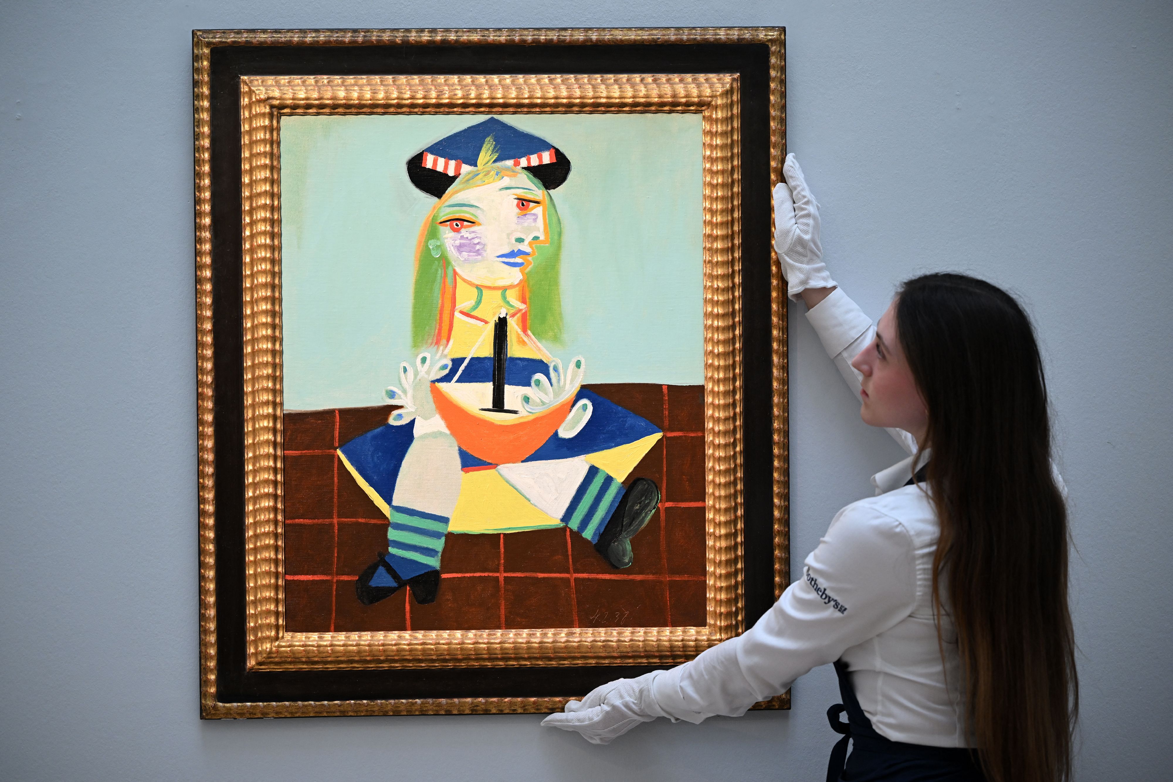 An employee works poses with an artwork entitled 'Fillette au bateau (Maya)' by Pablo Picasso, during a photo call at Sotheby's auction house in central London on February 22, 2023. - The painting is expected to realise in the region of USD 15-22 million dollars (EUR 14-20 million euros, GBP 12-18 million pounds) at auction in March. (Photo by JUSTIN TALLIS) (AFP)