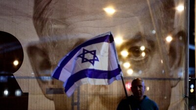 A man holds an Israeli flag as he stands in front of a large picture of Israeli Prime Minister Benjamin Netanyahu. (REUTERS)