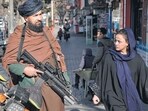 Taliban In Afghanistan: A Taliban fighter stands guard as a woman walks past in Kabul, Afghanistan. Taliban In Afghanistan: A Taliban fighter stands guard as a woman walks past in Kabul, Afghanistan.