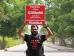 The image shows Kiran Verma holding up a placard to raise awareness about blood donation. 