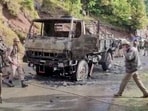 Armed security personnel walk at a site of an attack inspecting charred army vehicle in Poonch.