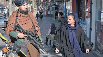 Afghanistan: A Taliban fighter stands guard as a woman walks past in Kabul, Afghanistan. Afghanistan: A Taliban fighter stands guard as a woman walks past in Kabul, Afghanistan.
