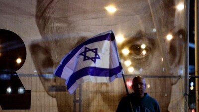 FILE PHOTO: A man holds an Israeli flag as he stands in front of a large picture of Israeli Prime Minister Benjamin Netanyahu. (REUTERS)