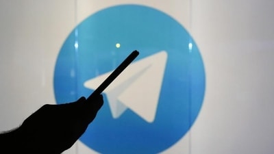 A man is seen as a silhouette as he checks a mobile device whilst standing against an illuminated wall bearing Telegram's logo in this arranged photograph in London. (Bloomberg)