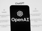 The OpenAI logo is seen on a mobile phone in front of a computer screen which displays the ChatGPT home Screen. . The OpenAI logo is seen on a mobile phone in front of a computer screen which displays the ChatGPT home Screen. .