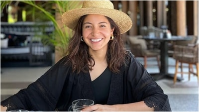 In this photo, Anushka sat at a table and posed with a beverage. The actor, dressed in a black outfit and a hat, smiled for the camera. (Instagram) In this photo, Anushka sat at a table and posed with a beverage. The actor, dressed in a black outfit and a hat, smiled for the camera. (Instagram)