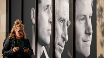 King Charles' Coronation: A woman walks past a poster with a portrait of King Charles III alongside William, Prince of Wales and Prince Harry in Central London. (AP)