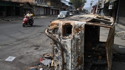 A motorist rides past a burnt vehicle on a street in Churachandpur in violence hit areas of northeastern Indian state of Manipur. (AFP)