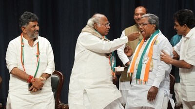 Congress president Mallikarjun Kharge offers sweets to Siddaramaiah during celebrations after the party's win in Karnataka Assembly elections, as state unit chief DK Shivakumar looks on. (PTI) Congress president Mallikarjun Kharge offers sweets to Siddaramaiah during celebrations after the party's win in Karnataka Assembly elections, as state unit chief DK Shivakumar looks on. (PTI)