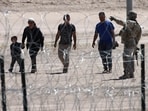 Migrants wait for U.S. authorities, between a barbed-wire barrier and the border fence at the US-Mexico border