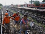 Workers walk on a rail track as a train arrives at Bahanaga Bazar railway station, near the site of the train collision.