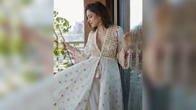 Nushrratt's ensemble features a long ivory jacket-style kurta with a deep v-neck, knot detailing, flared hem, and adorned with butti, pompom, tassels, thread, and mirror embroidery. It is paired with a matching white cotton skirt. (Instagram/@nushrrattbharuccha) Nushrratt's ensemble features a long ivory jacket-style kurta with a deep v-neck, knot detailing, flared hem, and adorned with butti, pompom, tassels, thread, and mirror embroidery. It is paired with a matching white cotton skirt. (Instagram/@nushrrattbharuccha)