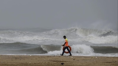 A lifegaurd walks along the sea-shore as waves crash onto the shore. (PTI)