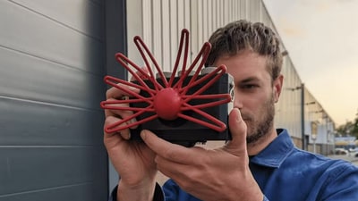 The camera features a crimson-hued, spider web-shaped TV-aerial-like attachment, complemented by three dials, a red shutter button, and a touch-sensitive viewfinder screen. (Bjørn Karmann) The camera features a crimson-hued, spider web-shaped TV-aerial-like attachment, complemented by three dials, a red shutter button, and a touch-sensitive viewfinder screen. (Bjørn Karmann)