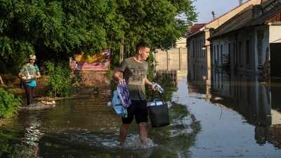 Local residents carry their belongings from a flooded house after the Nova Kakhovka dam breached, amid Russia's attack on Ukraine. (Reuters)