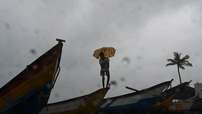 Cyclone Biparjoy: A man with an umbrella stands over fishing boats stationed along a beach. (AFP / Representative) Cyclone Biparjoy: A man with an umbrella stands over fishing boats stationed along a beach. (AFP / Representative)