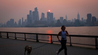 A woman jogs with a dog along the Hudson River shortly after sunrise, as haze and smoke caused by wildfires in Canada. (Reuters) A woman jogs with a dog along the Hudson River shortly after sunrise, as haze and smoke caused by wildfires in Canada. (Reuters)