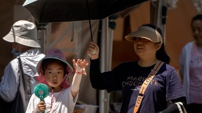 A girl uses a portable fan to keep herself cool as she walks past vendor booths at a Dragon Boat festival event at a public park on an unseasonably hot day in Beijing, Thursday. (AP) A girl uses a portable fan to keep herself cool as she walks past vendor booths at a Dragon Boat festival event at a public park on an unseasonably hot day in Beijing, Thursday. (AP)