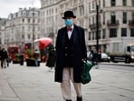 A pedestrian wearing a bow ties and bowler hat along with a face mask or covering due to the COVID-19 pandemic.