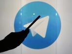 A man is seen as a silhouette as he checks a mobile device whilst standing against an illuminated wall bearing Telegram's logo. A man is seen as a silhouette as he checks a mobile device whilst standing against an illuminated wall bearing Telegram's logo.