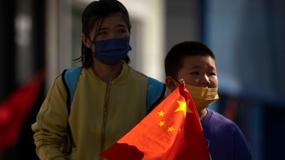 A boy wearing a face mask carries a Chinese flag as he walks along a pedestrian shopping street in Beijing. (AP) A boy wearing a face mask carries a Chinese flag as he walks along a pedestrian shopping street in Beijing. (AP)