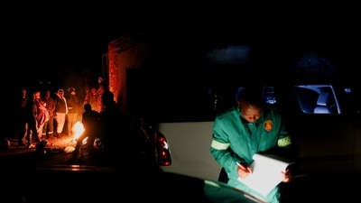 South Africa Gas Leak: A member of the Emergency Medical Services (EMS) writes notes as onlookers gather around a fire near the scene of a suspected gas leak. (Reuters)