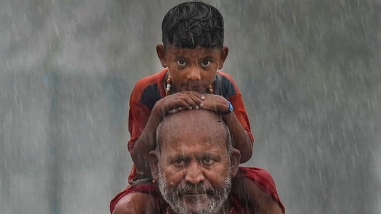 Kanwariya (Lord Shiva devotee) carring holy water from the Ganga walks with a kid amid heavy monsoon rains in the holy month of Sharvan, in New Delhi. (PTI)