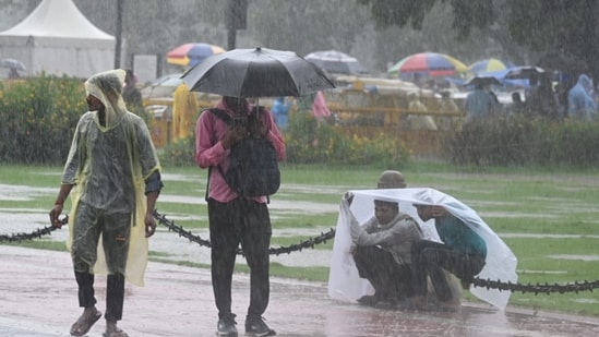 Commuters in raincoats and umbrellas amid rainfall in Delhi on Sunday. (Sanjeev Verma/ Hindustan Times)