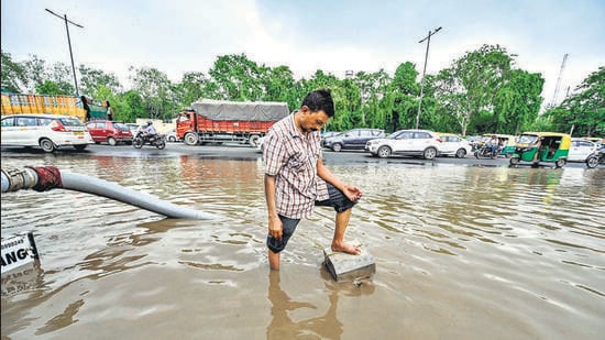A civic worker attempts to open choked drains on a waterlogged road at Pragati Maidan Ring Road in New Delhi on Monday. (Raj K Raj/HT Photo)