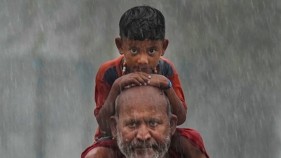 Kanwariya (Lord Shiva devotee) carring holy water from the Ganga walks with a kid amid heavy monsoon rains in the holy month of Sharvan, in New Delhi. (PTI)