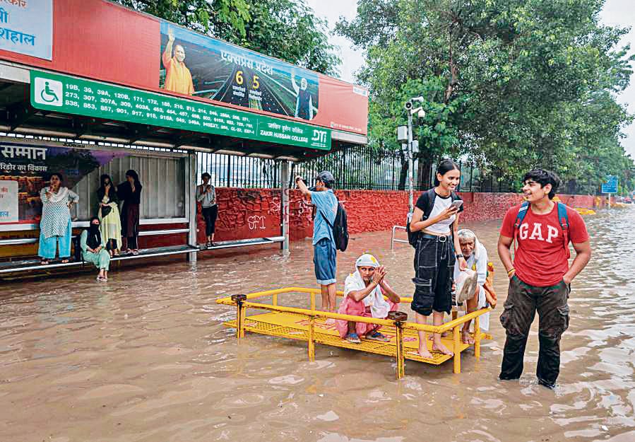 Rolling up their sleeves and pants, students wait at the Zakir Husain College bus stop to find their way back home. (Photo: Reuters) Rolling up their sleeves and pants, students wait at the Zakir Husain College bus stop to find their way back home. (Photo: Reuters)