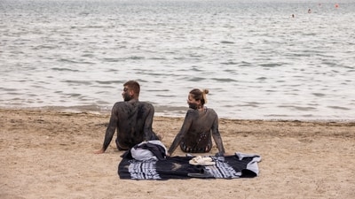 A couple covered in mud that is believed to be curative sit at the Queen's beach in Croatia. (Reuters)