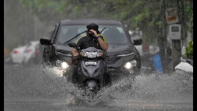 Commuters navigate through a waterlogged street after moderate rain lashed the city on Saturday. (Gurpreet Singh/HT)