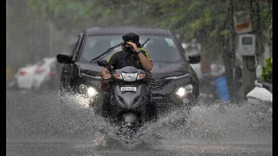 Commuters navigate through a waterlogged street after moderate rain lashed the city on Saturday. (Gurpreet Singh/HT)
