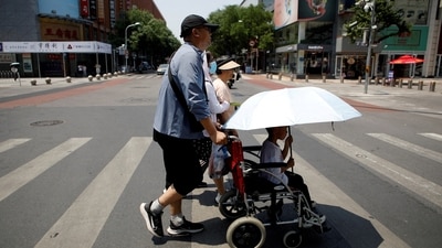 Pedestrians cross a road on a hot day amid an orange alert for heatwave, in Beijing (REUTERS)