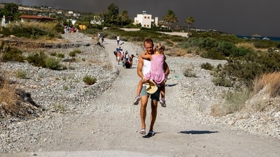 A man carries a child as they leave an area where a forest fire burns on the island. Volunteers fought to extinguish a blaze that blackened the hillside and charred buildings near Lindos.&nbsp; (AP)