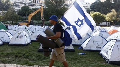 A protester carries an Israeli flag past protesters' tents during a demonstration in Jerusalem, Israel, on Monday. (Bloomberg) A protester carries an Israeli flag past protesters' tents during a demonstration in Jerusalem, Israel, on Monday. (Bloomberg)