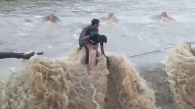 The two local teenagers held onto a railing as the river was overflowed due to incessant heavy rainfall. (Twitter/ANI)